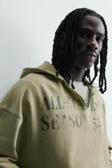 Sudadera de corte relajado color verde oliva con efecto lavado. Presenta capucha con abertura frontal, bolsillo tipo canguro, mangas largas con puños de rib y bajo con acabado irregular. Incluye estampado frontal con texto.