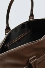 Bolso de viaje color marrón liso con acabado brillante. Cuenta con un compartimento principal con cierre de cremallera, un bolsillo interior con cremallera y un bolsillo frontal con cremallera. Tiene dos asas de mano y una correa de hombro ajustable y extraíble.