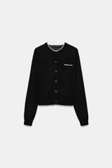 Chaqueta de punto de efecto doble capa color negro, con cuello redondo y ribete blanco, manga larga y cierre frontal con botones. Cuenta con un bolsillo de parche en el pecho con detalle en contraste.
