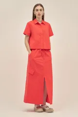 Falda larga color coral, estilo cargo, con cintura regulable con cordón, tajo frontal y bolsillos laterales con solapa.