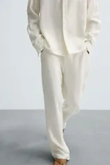 Pantalón de corte relajado confeccionado en tejido de cáñamo color blanco roto. Presenta cintura elástica con cordón interior ajustable, cierre frontal con botones, bolsillos laterales y un bolsillo trasero de plastrón.