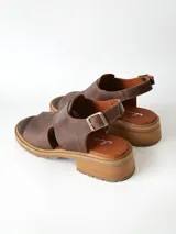 Sandalias de cuero color chocolate con suela track y taco bajo cuadrado. Poseen capellada cerrada con aberturas laterales y tira ajustable en el talón con hebilla metálica.