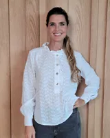 Blusa de manga larga color blanco con delicado estampado floral en relieve. Presenta un cuello alto con volados, cierre frontal parcial con botones y puños ajustados con botón.
