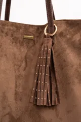 Bolso tipo tote de gran tamaño confeccionado en gamuza sintética color tostado. Presenta un diseño minimalista con asas largas de hombro y una pequeña placa metálica frontal con el logo de la marca.