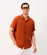 Camisa de manga corta color terracota, con cuello inglés y cierre frontal de botones, confeccionada en algodón con textura de corte comfort.