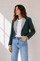 Chaqueta corta de paño en color verde petróleo, con solapas en contraste de color gris claro con textura sutil. Presenta un diseño estructurado con bolsillos frontales con solapa y cierre de un botón.