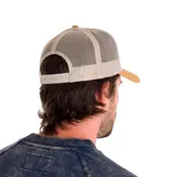 Gorro de hombre tipo trucker, con visera curva color mostaza y paneles frontales grises con logo de Caterpillar bordado. Paneles traseros de malla color beige y cierre ajustable a presión.