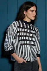 Blusa negra de algodón con detalles de franjas horizontales en encaje. Presenta cuello alto, mangas tres cuartos con terminación de volados en encaje y ajuste en la cintura con lazo del mismo tejido.