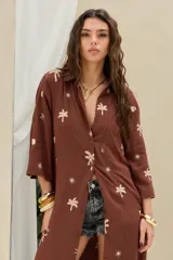 Camisola larga de color marrón con bordados en tono crudo de palmeras y soles, mangas largas y cierre frontal con botones.