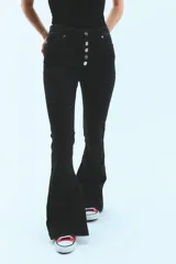 Jean negro de tiro medio alto, corte oxford con botamanga ancha y tajo. Cierre frontal con cinco botones metálicos.