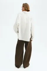 Camisa oversized blanca con finas rayas verticales beige, de manga larga y cierre frontal con botones.