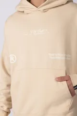 Buzo canguro color marrón con capucha, confeccionado en frisa de algodón. Presenta un diseño gráfico estampado en el frente con texto y logo circular, bolsillo tipo canguro y puños acanalados.