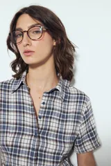 Camisa de manga corta con cuello camisero y botones frontales. Presenta un estampado de cuadros escoceses en tonos marrón oscuro y blanco/beige, con un calce entallado.