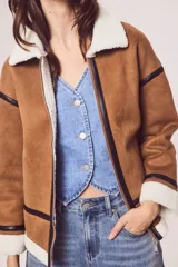 Campera marrón de gamuza sintética con cuello, puños y ruedo de piel sintética blanca. Presenta cierre frontal con cremallera, bolsillos laterales y detalles en cuero sintético negro.