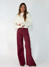 Pantalon de corte wide leg en color bordó, confeccionado en tejido de algodón. Presenta tiro medio, cierre frontal con botón y cremallera, bolsillos laterales y traseros, y un acabado deshilachado en el ruedo.