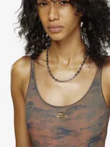 Traje de baño enterizo con diseño de camuflaje en tonos verdes y marrones. Presenta un corte cavado, escote redondo y un detalle metálico con el logo de la marca en el centro del pecho.