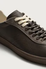 Zapatilla deportiva de estilo retro, confeccionada en una combinación de piezas de cuero texturizado y gamuza en tonos marrones. Presenta un diseño de doble cordonera con cordones claros y suela de goma a tono.