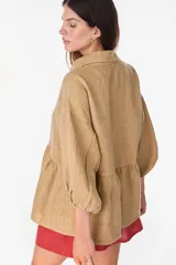 Camisa de lino marrón oscuro con silueta holgada, cuello camisero, cierre frontal de botones claros, mangas voluminosas y detalle de frunces en la cintura.