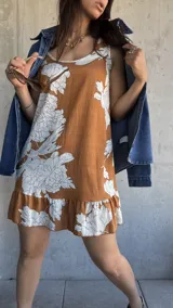 Vestido corto color camel con estampado de flores blancas, sin mangas, con cuello redondo y volados en el ruedo.