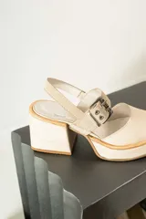 Zapato de tacón cuadrado y plataforma, color beige, con punta cerrada y tira ajustable con hebilla metálica en el tobillo.