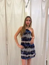 Vestido corto con escote halter y cuello alto, con tiras ajustables en el cuello. Presenta un diseño estampado con efecto tie-dye en tonos azul, negro y blanco, con espalda abierta y elástico en la cintura.