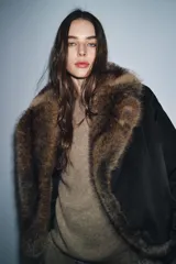 Chaqueta bomber negra de corte corto y diseño abullonado, con cuello de solapa amplio en pelo sintético marrón. Cuenta con mangas largas y cierre frontal.