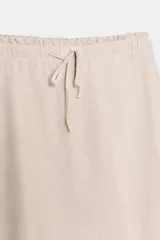 Falda midi de tiro alto, color beige claro, confeccionada en lino 100%. Presenta cintura elástica ajustable con cordones anudados al frente.