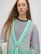 Cardigan oversize de algodón con diseño tejido a rombos en tonos degradados de marrón y blanco. Presenta cuello en V, cierre frontal con botones de madera y puños y dobladillo con rayas blancas.