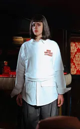Remera blanca de manga larga superpuesta a una camisa blanca de manga larga, ambas con cuello. La prenda exterior tiene un estampado frontal en naranja con texto censurado inspirado en la película Pulp Fiction.
