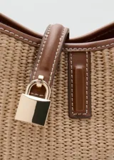 Bolso tipo bucket de canvas y efecto piel, con base, asas y detalles en marrón. Cuenta con una trabilla frontal con candado metálico dorado y cierre magnético.