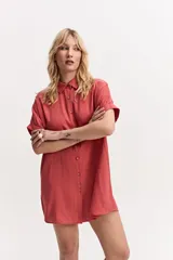 Vestido camisero corto color coral, de silueta amplia y suelta, con manga corta, cuello clásico y cierre frontal de botones.