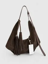 Cartera tipo hobo de textura gamuzada en color marrón oscuro, con diseño flexible y asa larga regulable. Presenta un detalle de flecos largos desmontables en uno de los laterales y cierre superior.