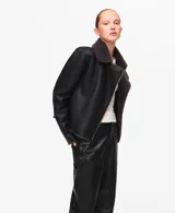 Chaqueta estilo aviador de color negro con interior de piel sintética gris oscuro, cierre frontal cruzado con cremallera y solapas grandes.