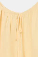 Blusa de lino color amarillo pastel, con escote recto ajustable mediante lazadas, hombros descubiertos y mangas largas abullonadas con puños elásticos.