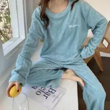 Conjunto de pijama de dos piezas confeccionado en tela de plush texturizada con diseño de rayas verticales en relieve. Incluye una remera de manga larga con cuello redondo y un pantalón de corte holgado. La remera presenta un pequeño bordado decorativo en el pecho.