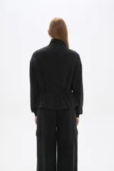 Campera negra de manga larga con cierre frontal, bolsillos frontales con solapa y cordón ajustable en la cintura.