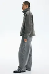 Campera de denim de algodón rígido, color gris oscuro con efecto gastado, cuello clásico, hombros caídos y cierre frontal. Cuenta con bolsillos delanteros ribeteados, un bolsillo superior con cierre y bajo recto.
