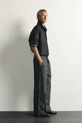 Pantalón relaxed fit de mezclilla con mezcla de algodón y lino, con diseño de rayas verticales oscuras y claras. Cuenta con cintura ajustable con cordón, bolsillos frontales, bolsillo cerillero y cierre frontal con cremallera y gancho metálico.