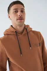 Buzo de algodón color marrón con capucha, bolsillo tipo canguro, mangas largas y logo estampado en el pecho.