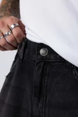 Jean de corte mom oversize, color negro lavado, con diseño de cinco bolsillos y cierre frontal con botón y cremallera.