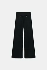 Pantalón de tiro medio confeccionado en tejido bouclé con hilos metalizados. Presenta pierna ancha, cintura elástica y falsos bolsillos de vivo decorados con botones dorados en la parte frontal.