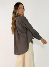 Camisa de corte oversize y diseño holgado, con cuello camisero, cierre frontal de botones y mangas largas con puños abotonados. Presenta un ruedo redondeado y una caída fluida.