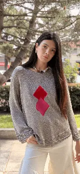 Buzo de lurex plateado brillante con diseño holgado, cuello redondo, mangas largas y rombos bordados en contraste en colores fucsia y rojo en el frente.