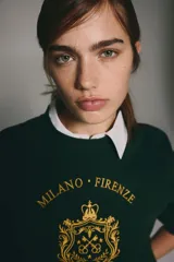 Buzo verde oscuro con cuello redondo, hombros caídos y un diseño frontal dorado que incluye una corona, un escudo y las palabras "Milano Firenze" y "La moda dal cuore". Tiene remates acanalados en cuello, puños y bajo, y un interior cepillado suave.