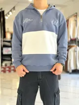 Hoodie de felpa con capucha y medio cierre frontal, diseño en bloques de color celeste y blanco, con bordados decorativos en el pecho.