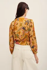 Camisa tipo cruzada (wrap) de manga larga con estampado floral multicolor en tonos mostaza y bordó. Cuenta con escote en V cruzado y detalle de lazo lateral con flor aplicada.