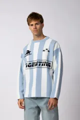 Sweater de tejido de punto con diseño a rayas verticales en color celeste y blanco. Presenta un corte holgado, cuello redondo y detalles gráficos en negro en el frente, incluyendo la palabra 'Argentina' y estrellas bordadas.
