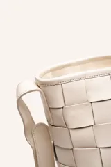 Cartera tipo morral de cuero color beige, con diseño trenzado artesanal, correa larga regulable y cierre superior.