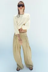 Pantalón de tiro medio color beige perteneciente a la colección ZW Collection, de corte ancho y recto, con detalle de pliegues frontales y cierre con cremallera y ganchos metálicos.