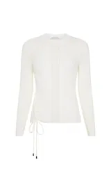 Sweater de punto fino color blanco, con cuello redondo y mangas largas. Presenta una textura acanalada con diseño de puntadas variadas y un detalle lateral de cordones trenzados con cierre de lazo y punteras metálicas.